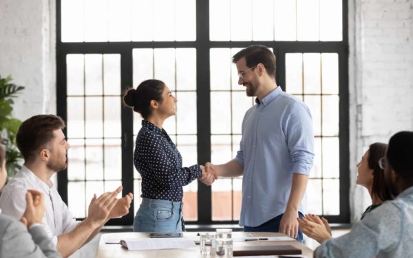 Indian and caucasian business people shake hands start negotiations with partners at boardroom. Staff cheering best employee of month receive praises, gratitude from boss, worker get promotion concept