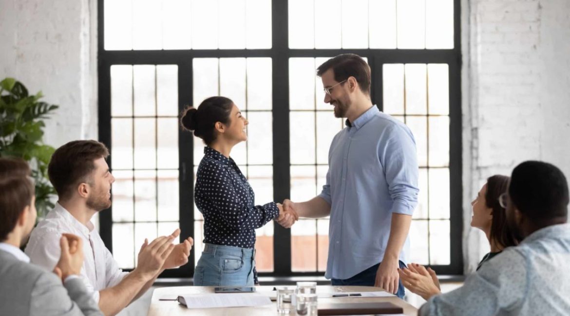 Indian and caucasian business people shake hands start negotiations with partners at boardroom. Staff cheering best employee of month receive praises, gratitude from boss, worker get promotion concept