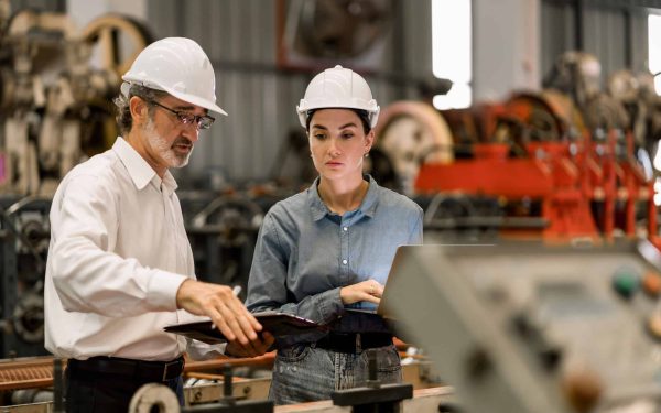 professional engineer,worker,technician use clipboard discuss work, walk in steel metal manufacture factory plant industry. Black African American man and woman wear hard hat check quality machine