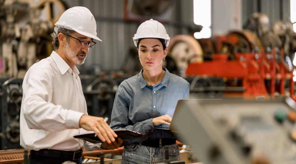 professional engineer,worker,technician use clipboard discuss work, walk in steel metal manufacture factory plant industry. Black African American man and woman wear hard hat check quality machine